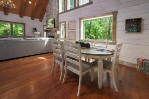 A wooden dining table with chairs, a sofa, and a large window with a view of trees.