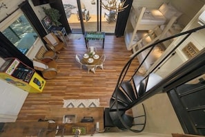 Um interior moderno com escada em espiral, piso de madeira, área de refeições com mesa e cadeiras e vista através de uma porta de vidro.
