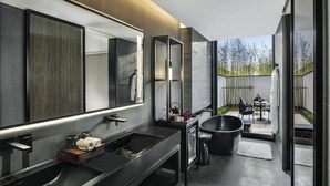 Un baño moderno con un espejo grande, encimeras negras y una bañera negra.