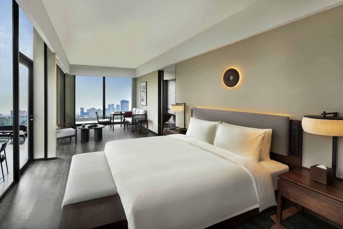 Una habitación de hotel moderna con una cama grande, un escritorio, una silla y vistas al horizonte de la ciudad.