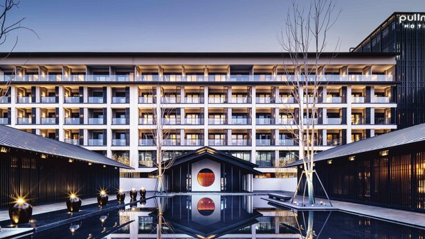 Un hotel moderno con una fachada simétrica, varios balcones y una piscina reflectante central.