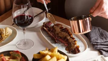 A dining table with a steak, a glass of red wine, and a plate of fries.