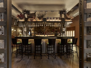 Eine Bar mit einer zentralen Theke, mehreren Barhocker, hängendem Glas und einer Auswahl an Flaschen.