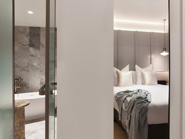 Ein modernes Schlafzimmer mit Bett, Nachttisch und einem Badezimmer mit Waschbecken und Spiegel.