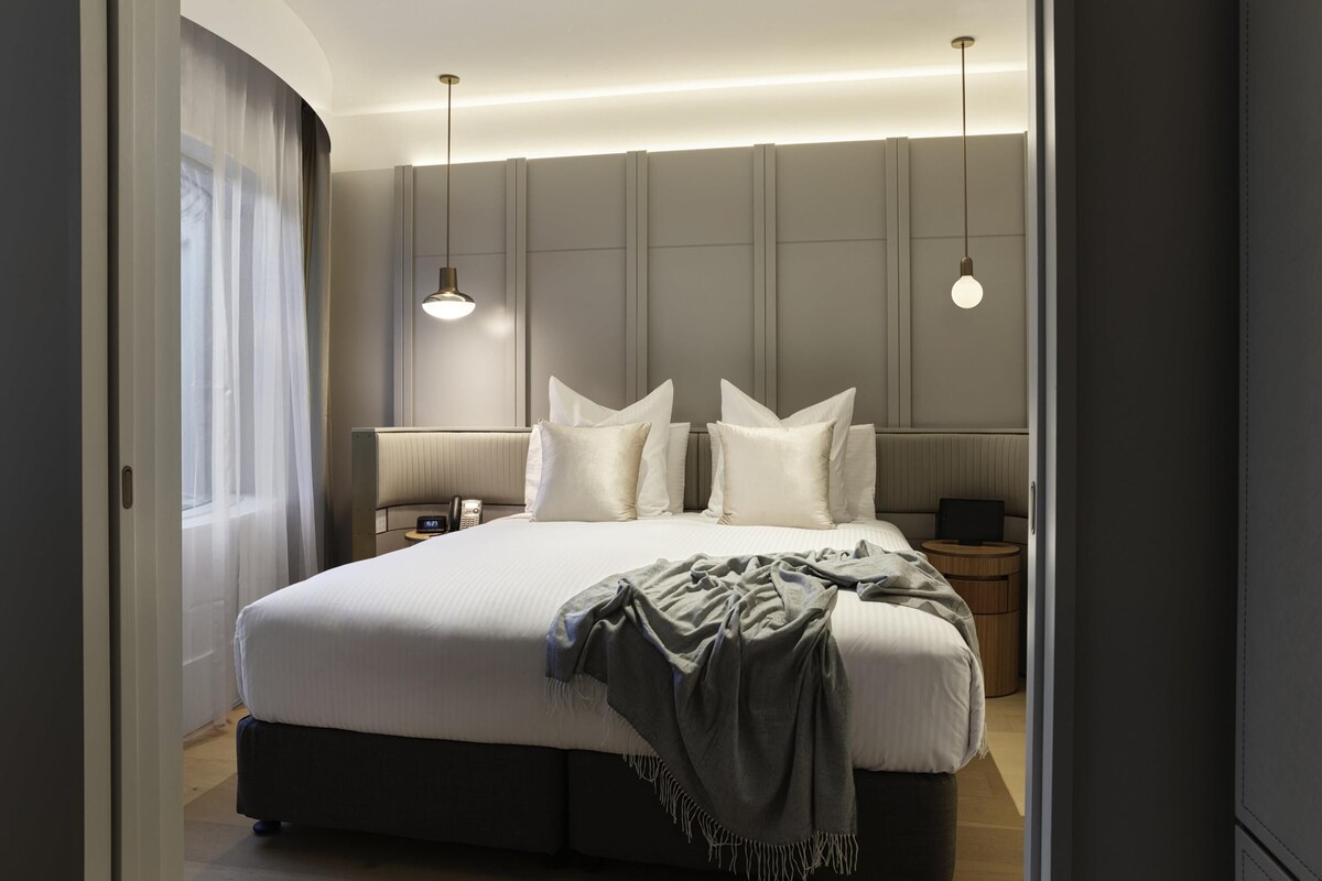 Une chambre d’hôtel moderne avec un grand lit, des tables de chevet, un téléphone et des lampes suspendues.
