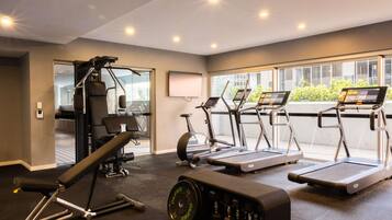 Een sportschool met loopbanden, een hometrainer en een gewichtbank.