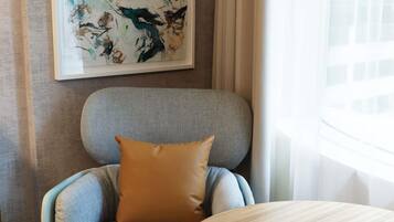 A room with a grey upholstered armchair, a round wooden table with a glass, a notebook, and a pen.