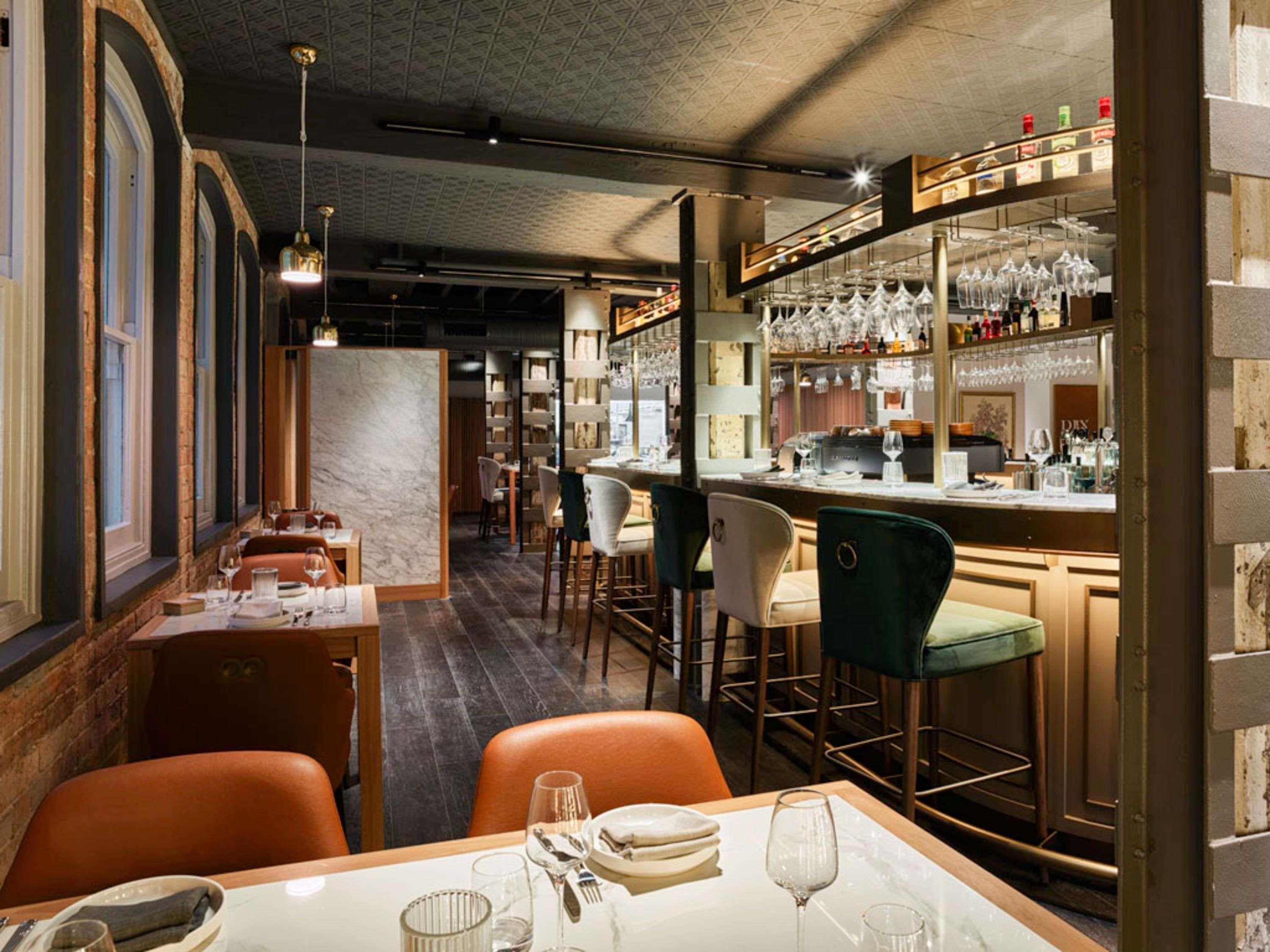 A restaurant interior with bar seating, marble columns, and hanging wine glasses.