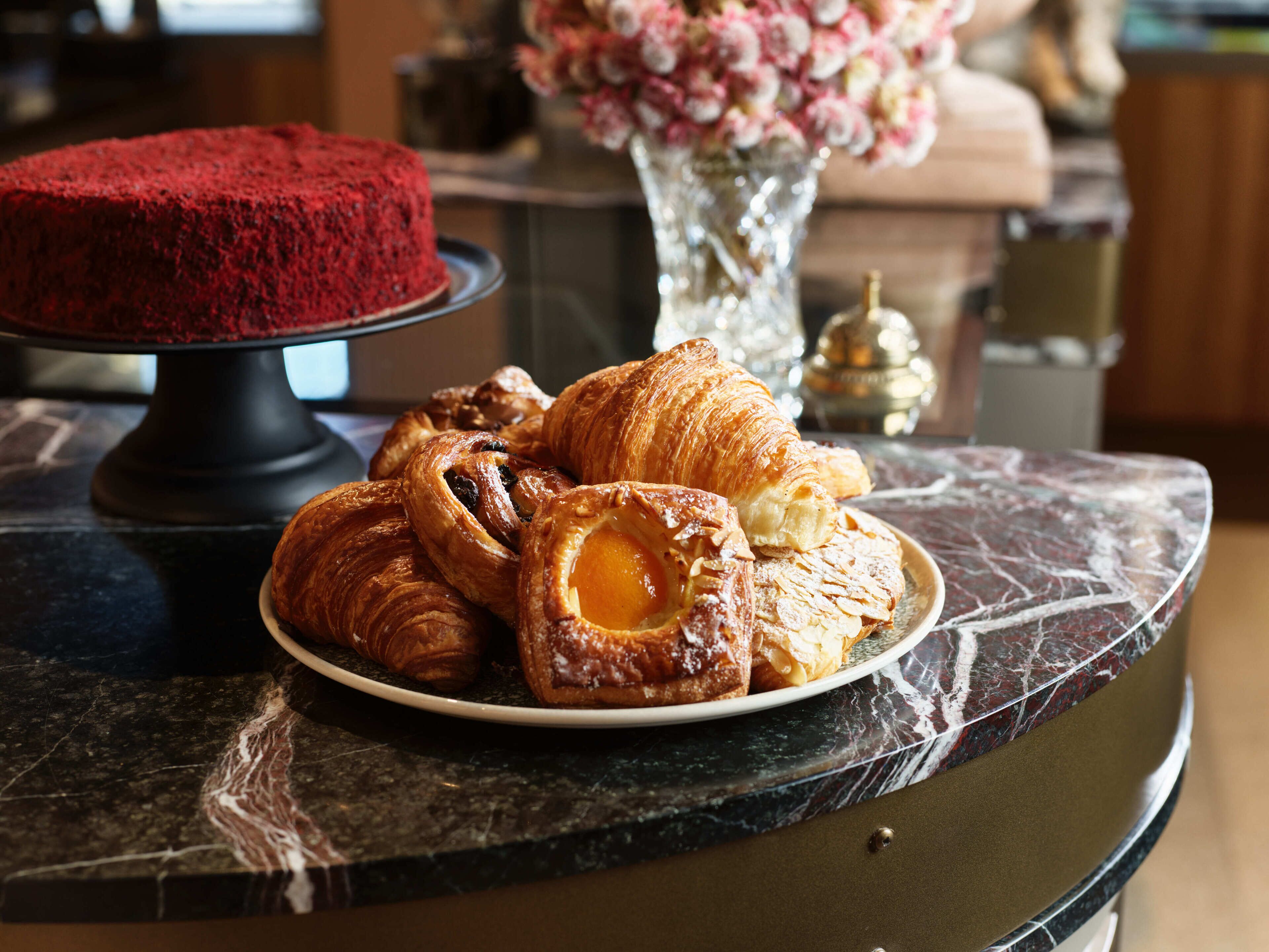 Une table en marbre sur laquelle se trouve une assiette de pâtisseries et un présentoir avec un gâteau rouge.