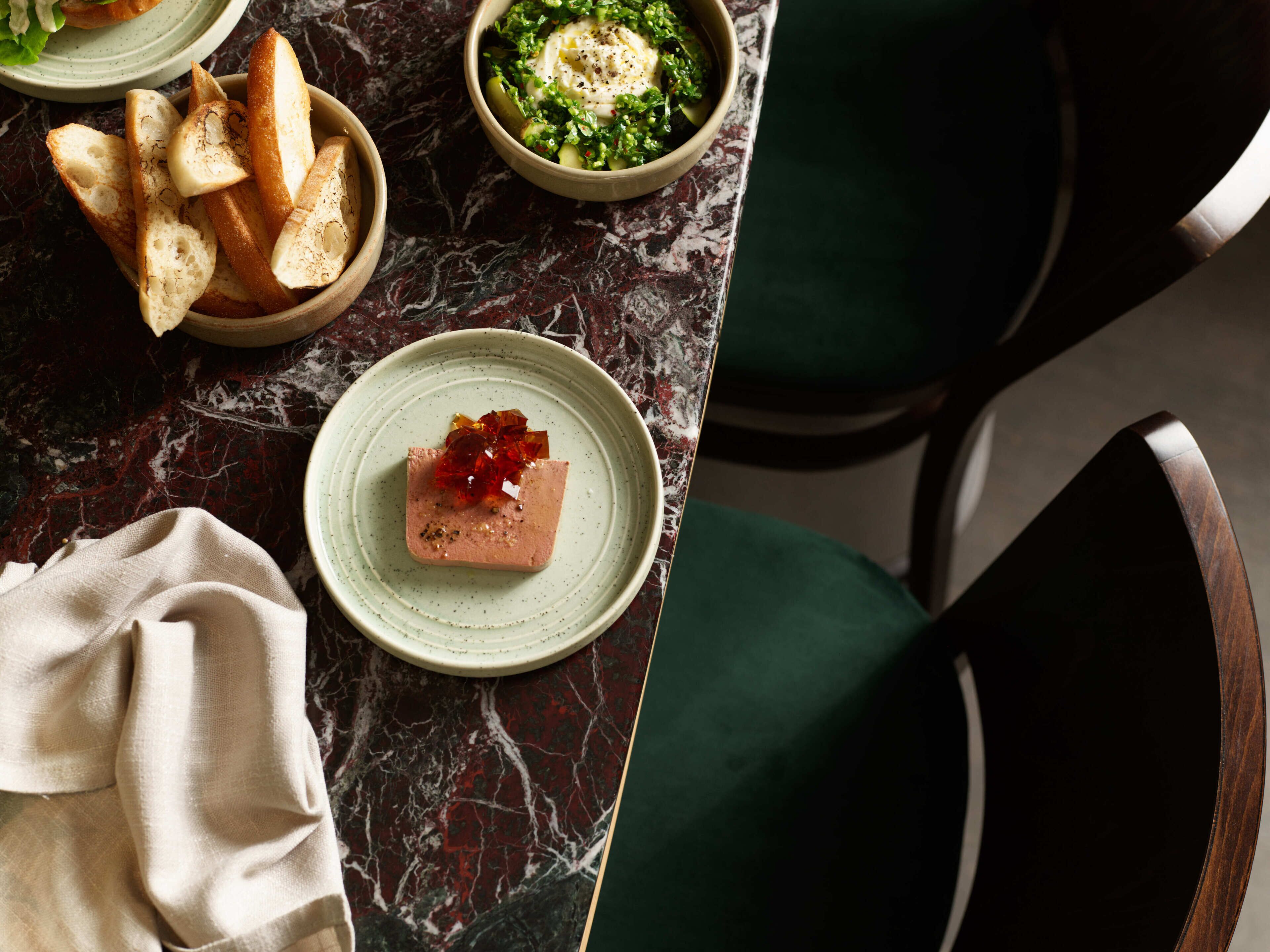 Une table à manger avec une assiette de nourriture, un bol de pain et une chaise verte.