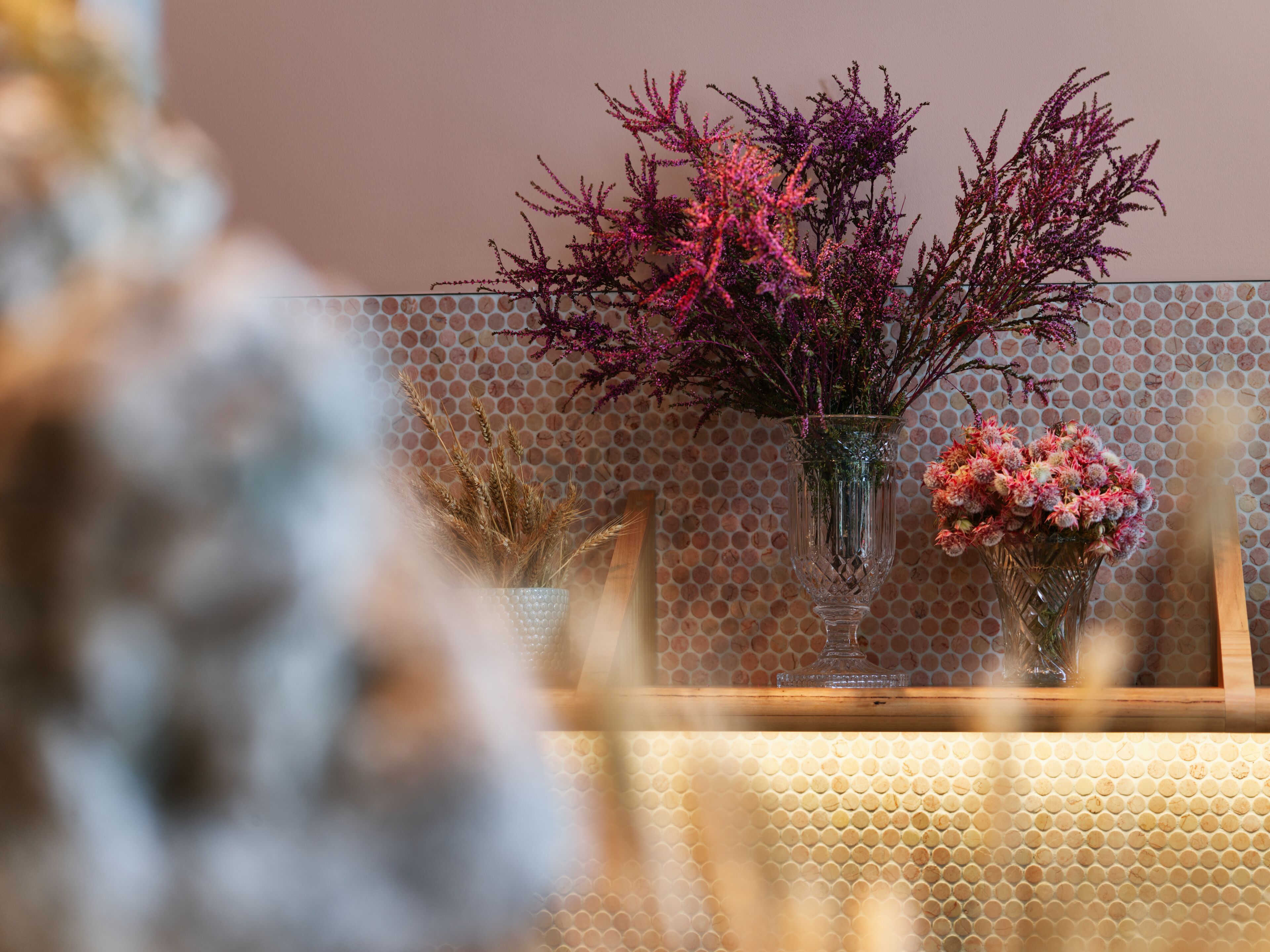 A room with a honeycomb-patterned wall and three vases with dried plants and flowers.