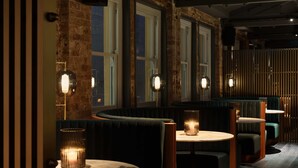 Hämärästi valaistu ravintola, jossa on tiiliseinät, suuret ikkunat ja pyöreät pöydät jakkaroineen.