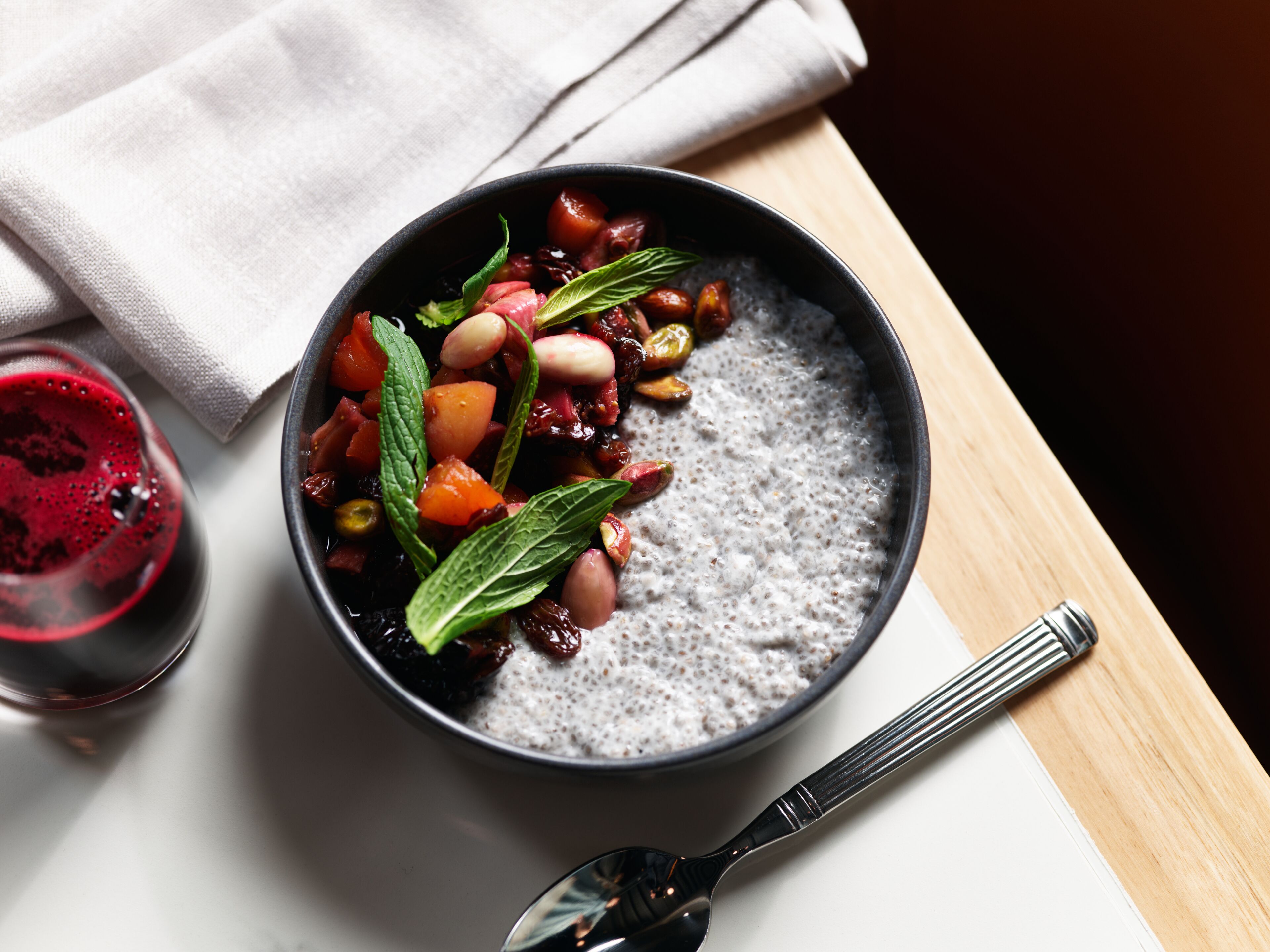 Un tazón de pudín de chía con frutos rojos y nueces, una copa de vino tinto y una cuchara sobre una mesa de madera.