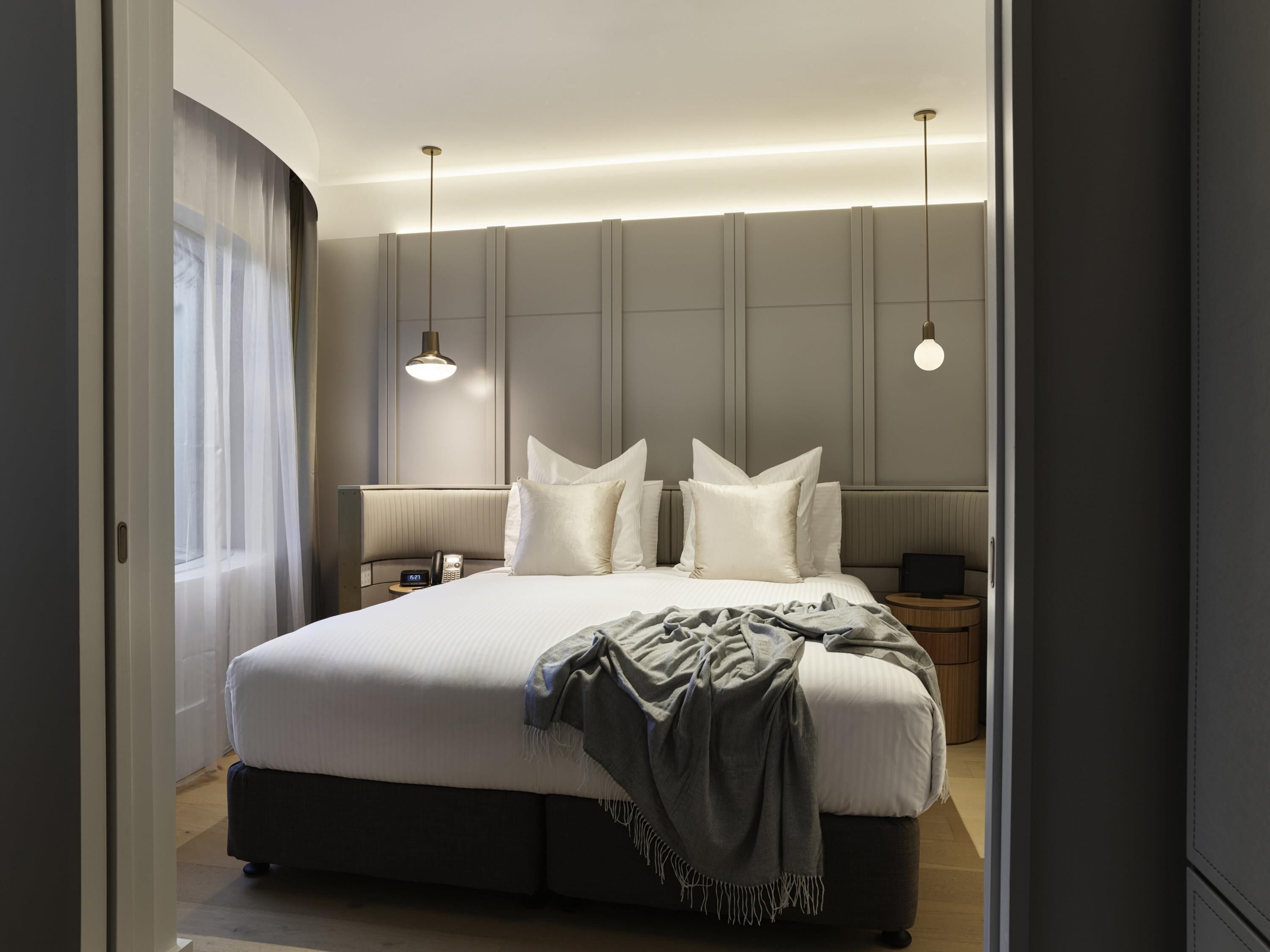 Une chambre d’hôtel moderne avec un grand lit, des tables de chevet, un téléphone et des lampes suspendues.