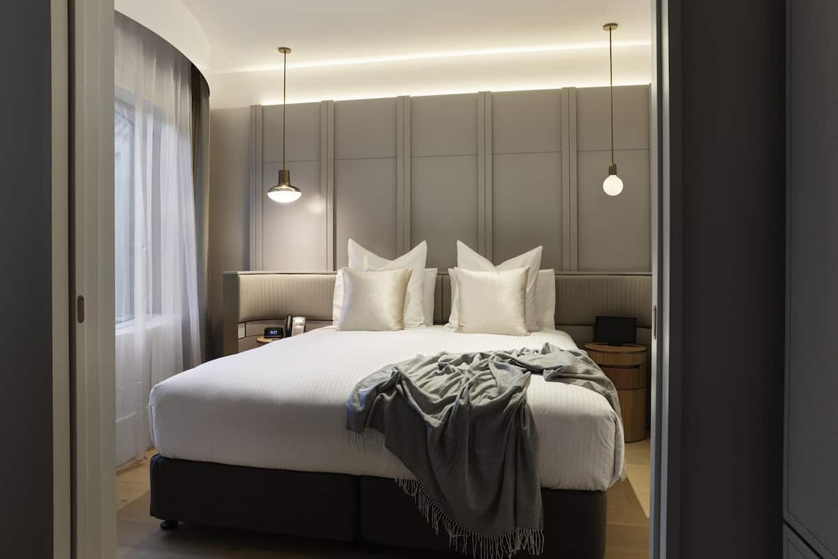 Une chambre d’hôtel moderne avec un grand lit, des tables de chevet, un téléphone et des lampes suspendues.