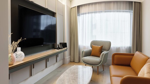 Een moderne woonkamer met een flatscreen televisie, een bank, een fauteuil en een salontafel.