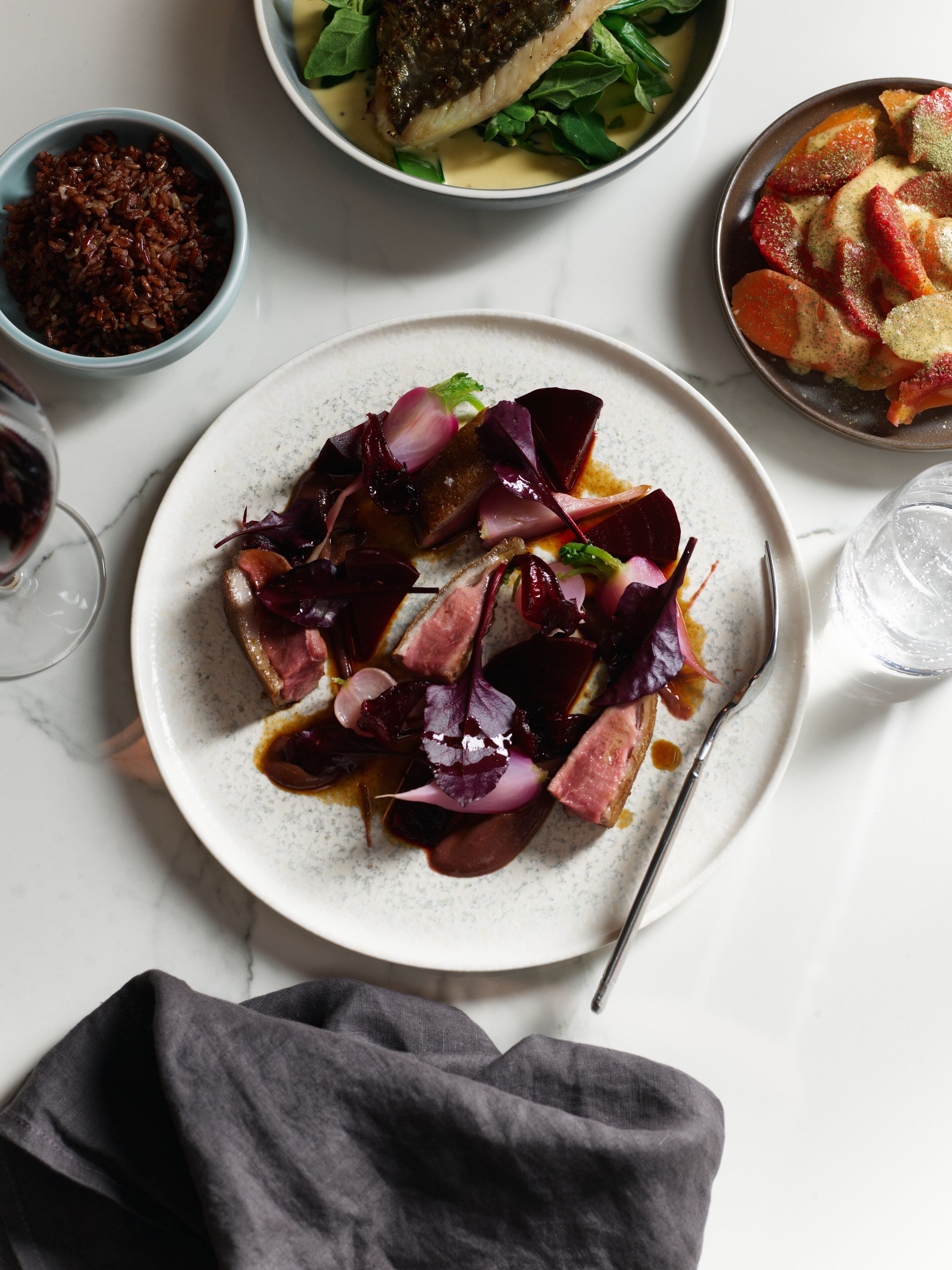 A dining table with a plate of food, a bowl of red rice, and a glass of water.