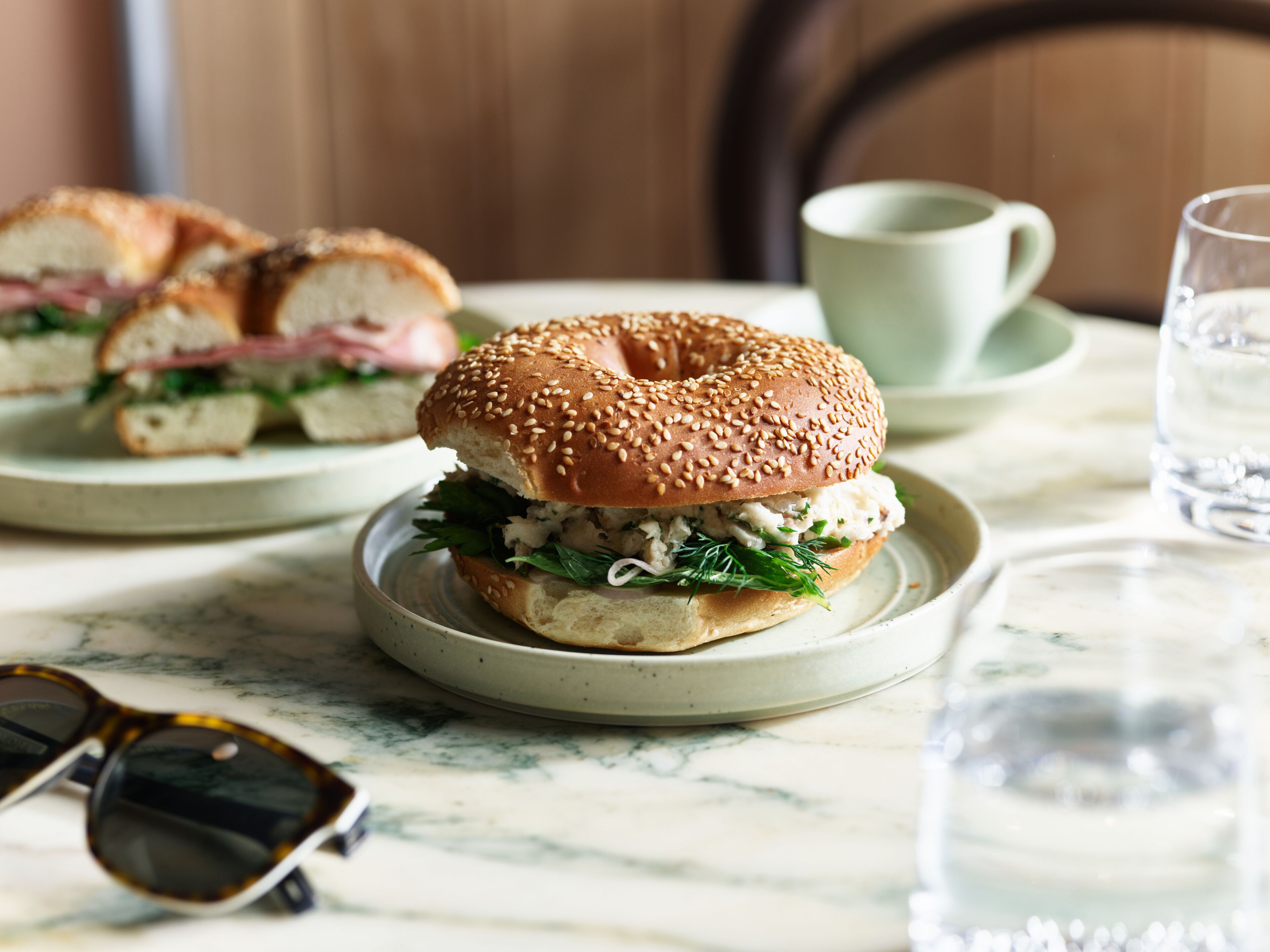 A sandwich on a plate with a cup and a glass of water on a table.