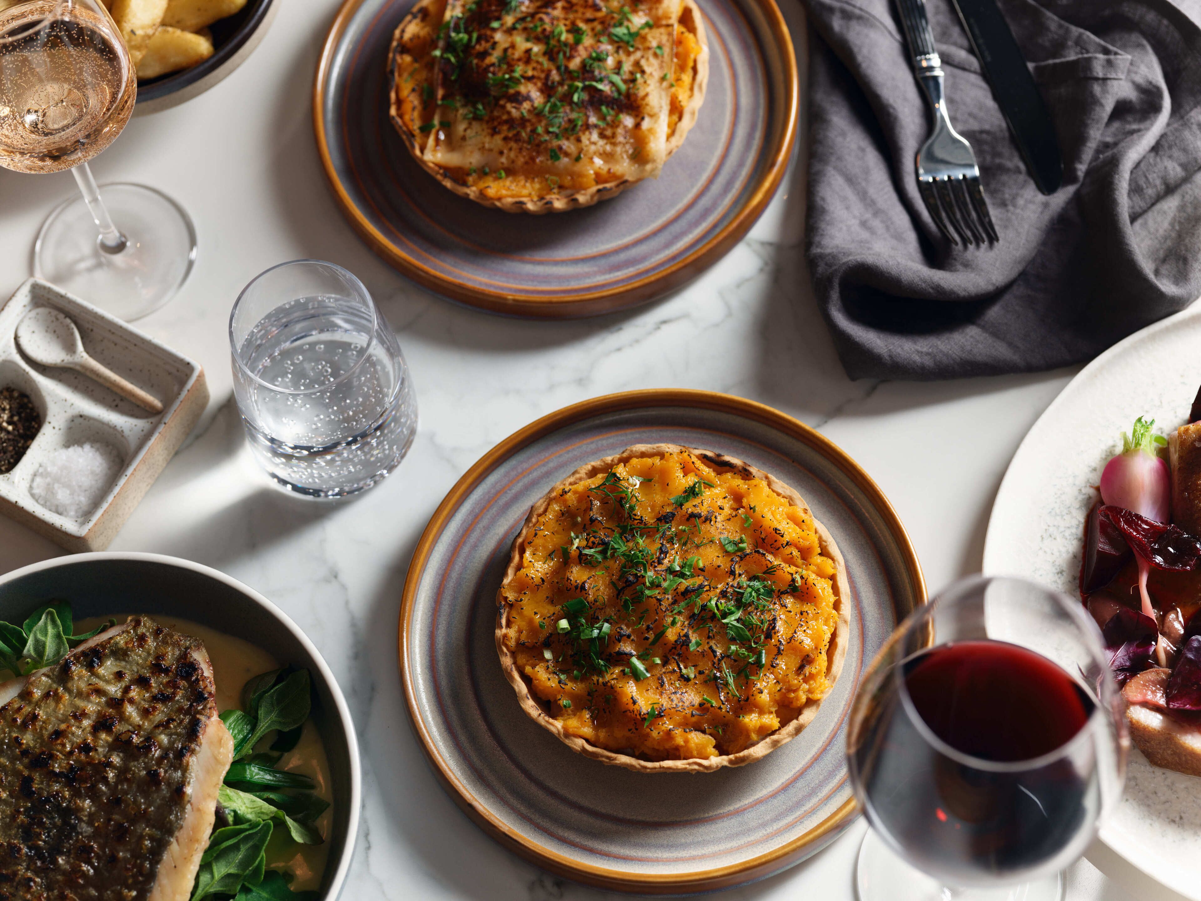 A dining table with a variety of dishes, including a quiche, a steak, and a glass of red wine.
