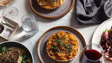 A dining table with a variety of dishes, including a quiche, a steak, and a glass of red wine.