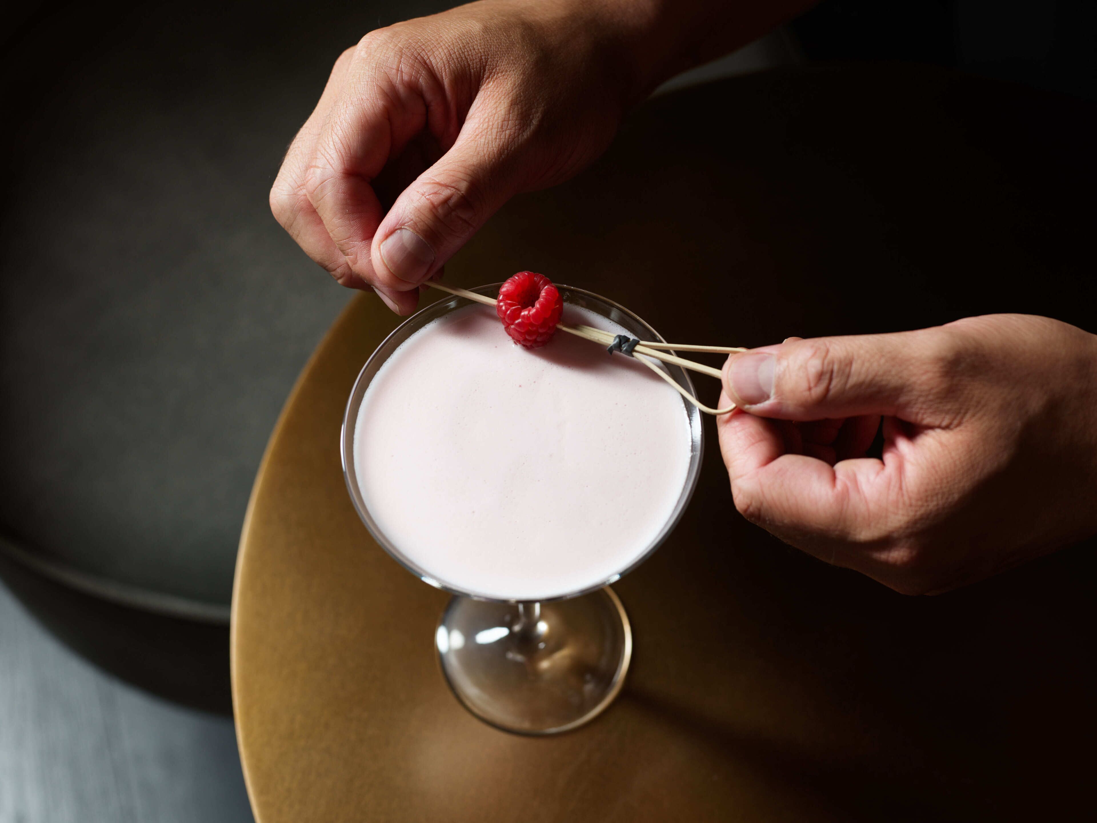 Eine Person hält einen Cocktail mit einer Himbeere als Dekoration.