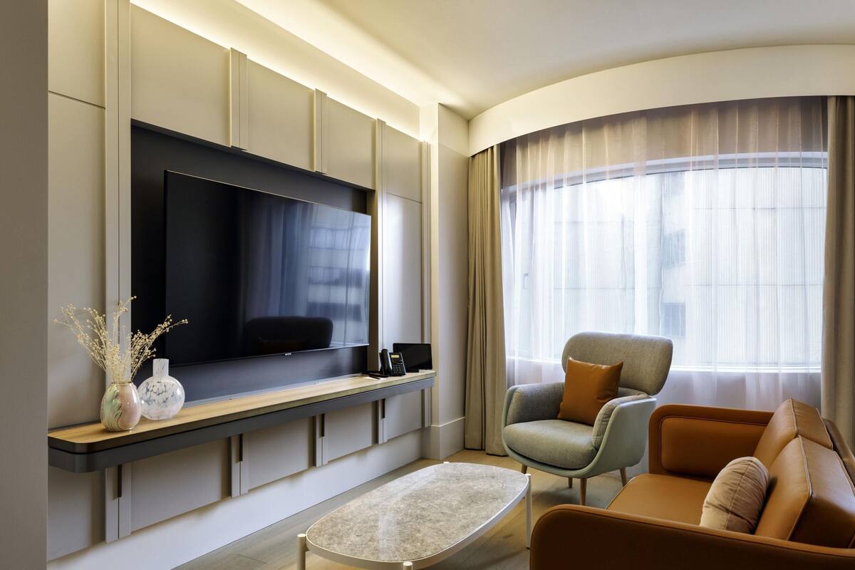 Een moderne woonkamer met een flatscreen televisie, een bank, een salontafel en een groot raam met gordijnen.
