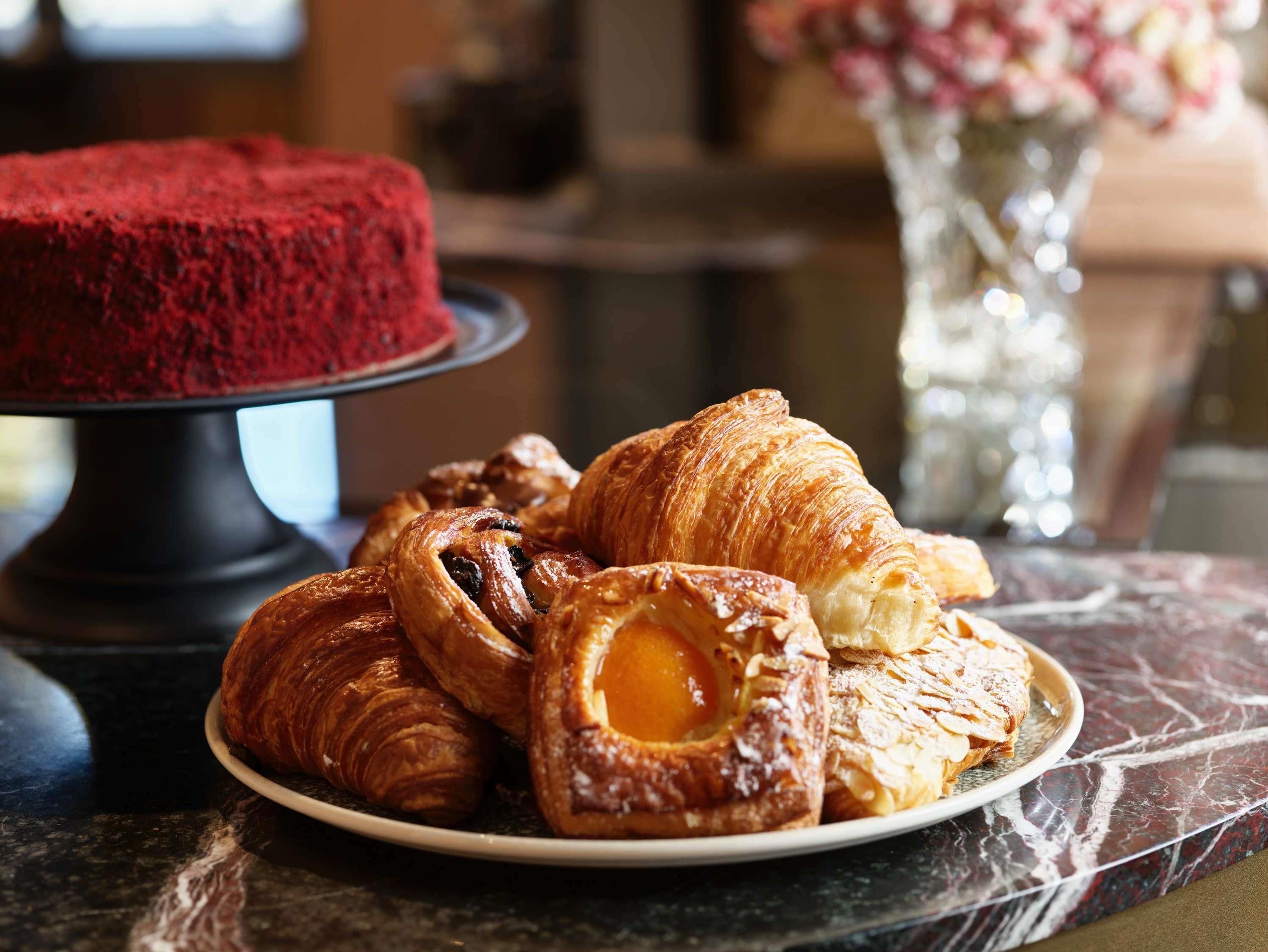 A plate of pastries and a red cake on a marble table.