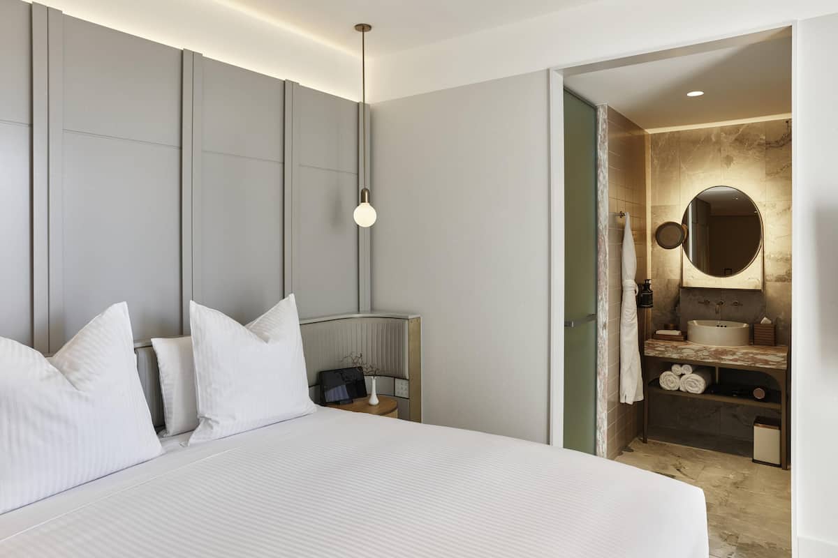 Ein modernes Hotelzimmer mit einem großen Bett, Nachttisch und einem Badezimmer mit Marmorwaschbecken und Spiegel.