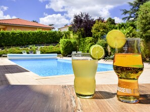 A poolside setting with a glass of a yellow beverage and a bottle of Brasserie D'Or wine. - Ibis Budget Millau Viaduc  (Millau)