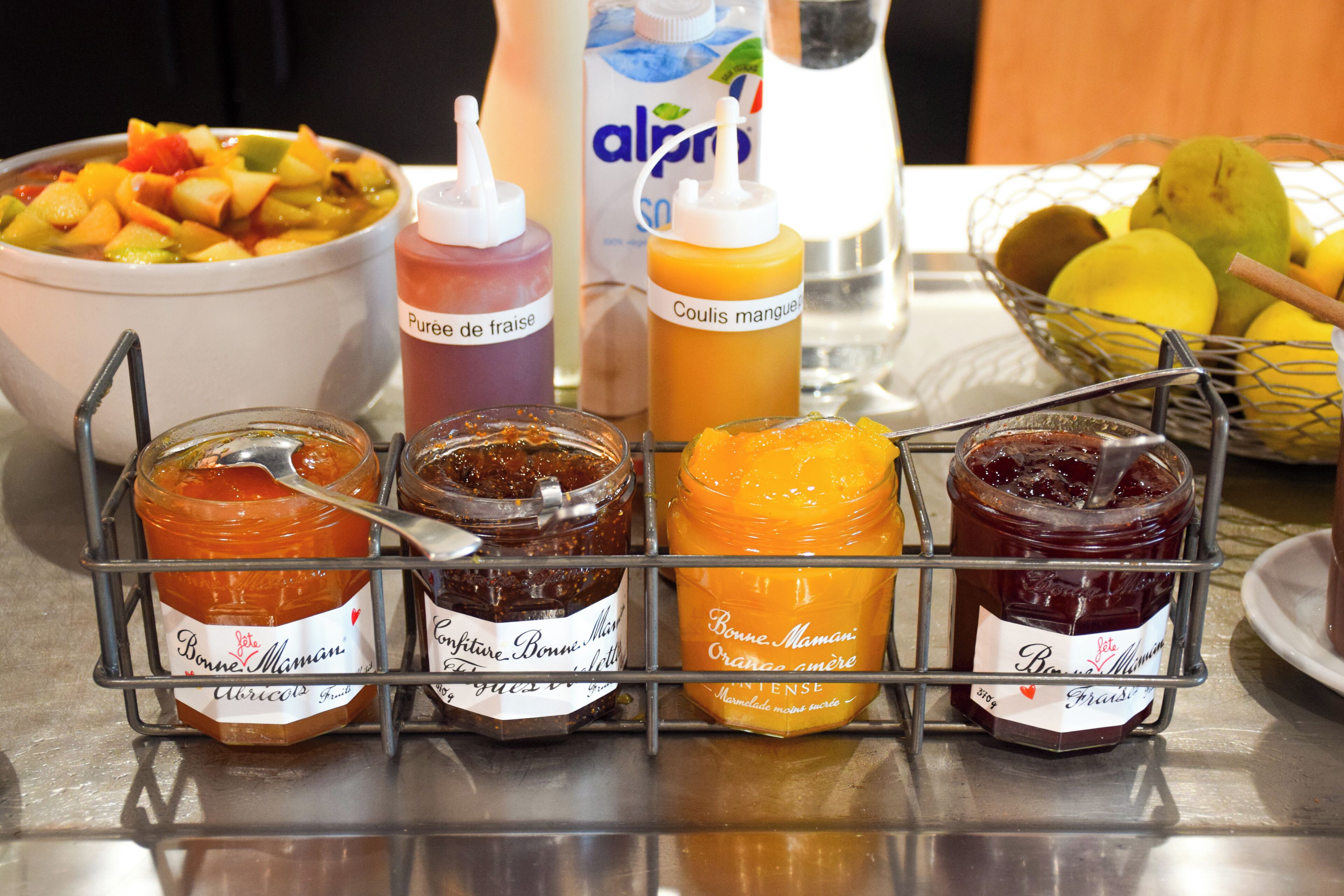 A breakfast table with various jams, a bowl of fruit salad, and a basket of lemons.