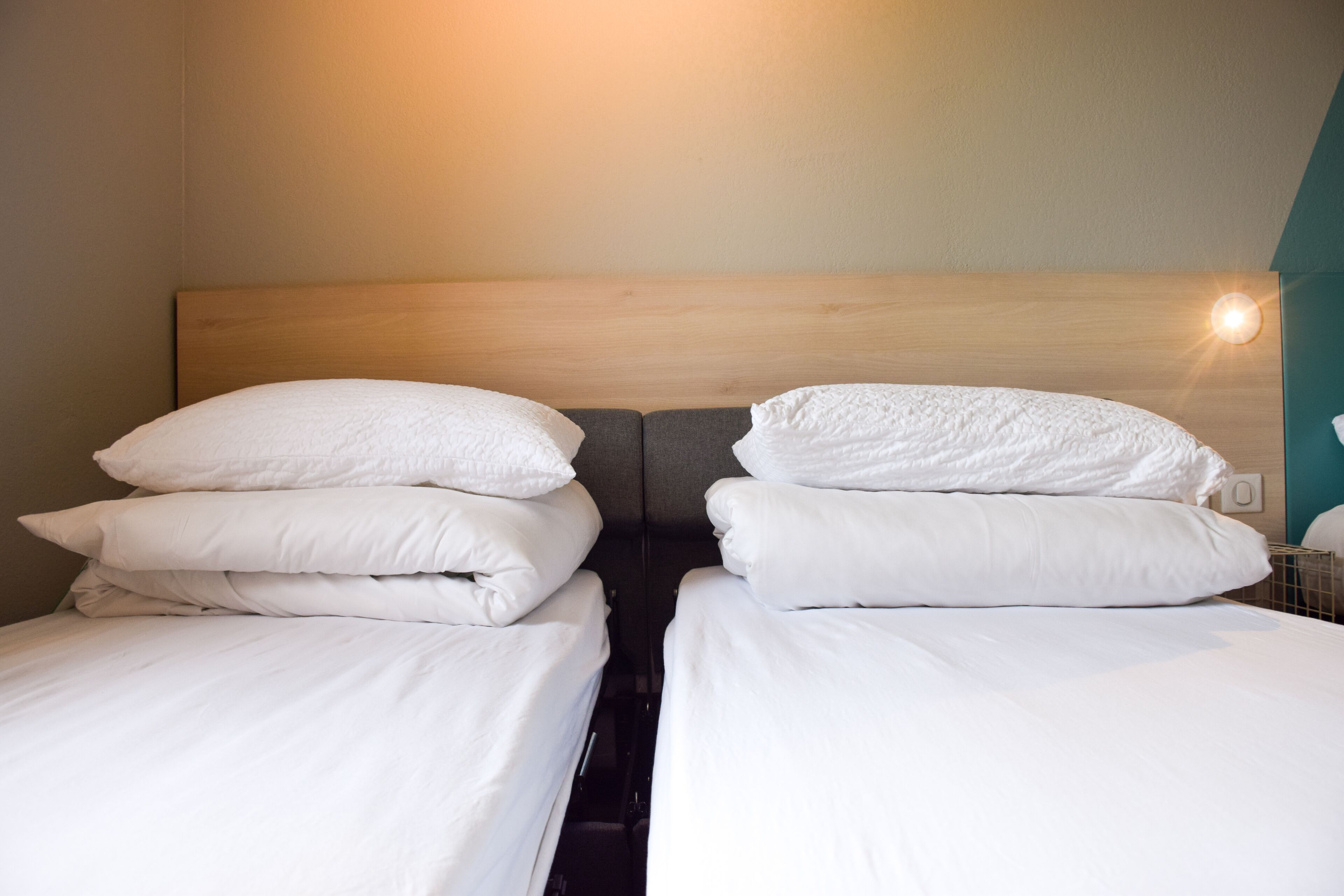 Un lit double avec une literie et des oreillers blancs, une tête de lit en bois et un luminaire fixé au mur.