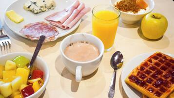 Une table de petit-déjeuner avec divers aliments, notamment une gaufre, des fruits, un verre de jus d’orange et un bol de yaourt.