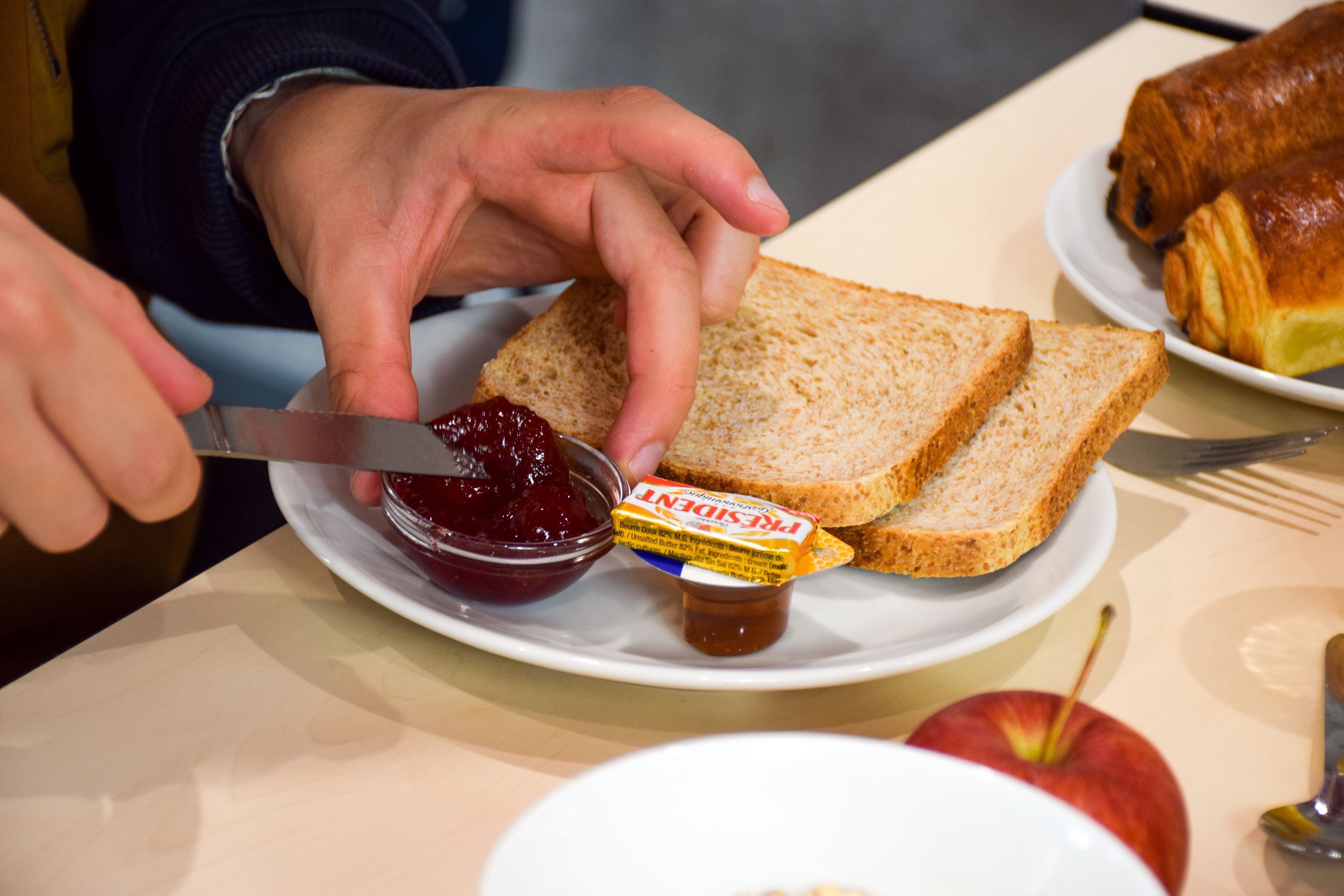 A plate with two slices of bread, a jar of jam, and a butter knife.
