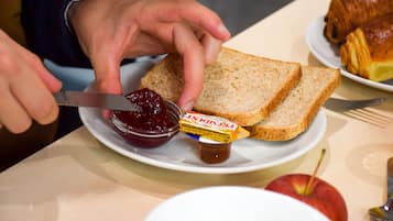 A plate with two slices of bread, a jar of jam, and a butter knife.