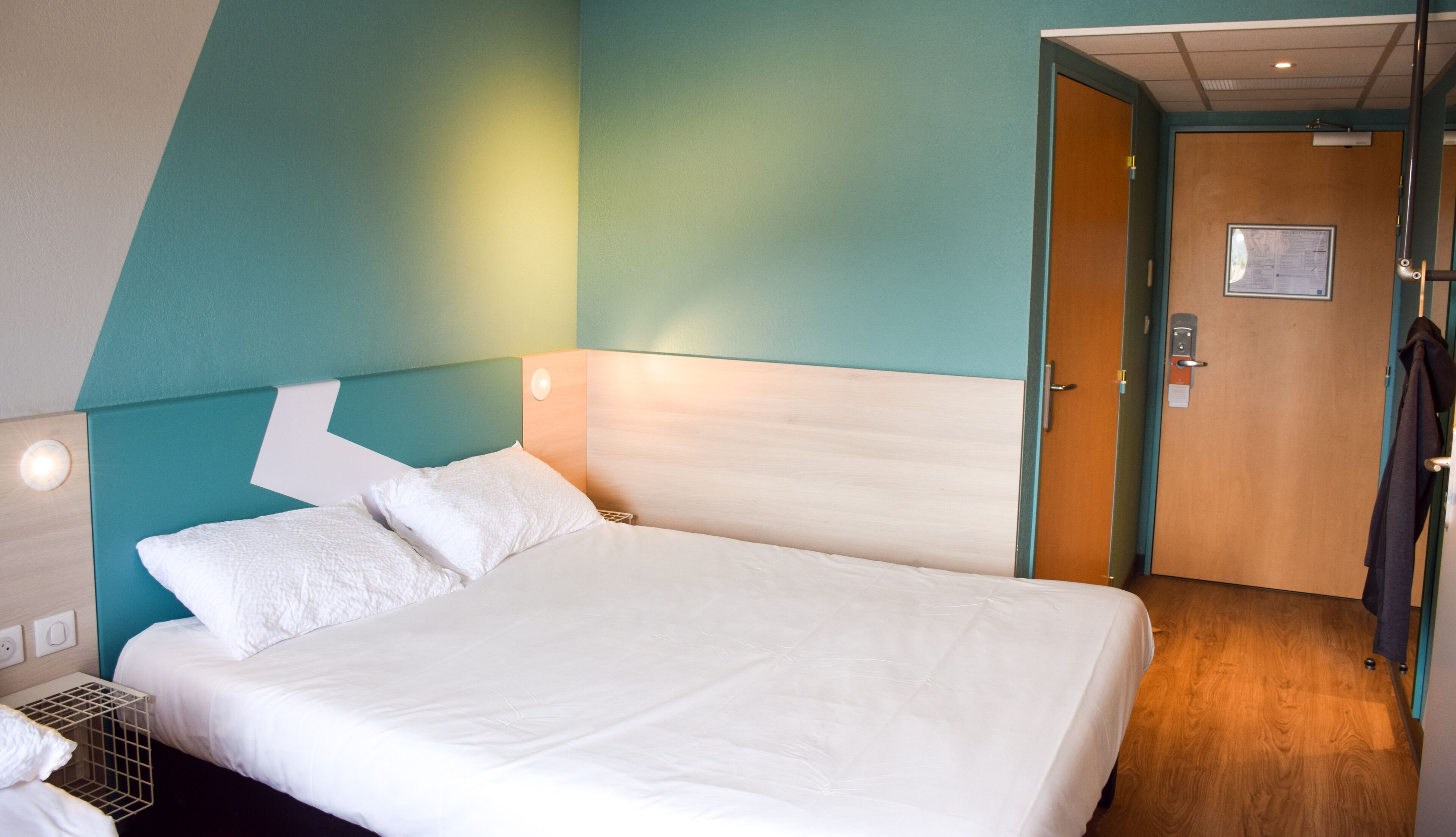 Et hotelværelse med en stor seng, et træhovedgærde og teal vægge.