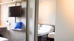 A hotel room with a bed, a TV mounted on the wall, a minibar, and a bathroom with a sink and mirror. - Ibis Budget Millau Viaduc  (Millau)
