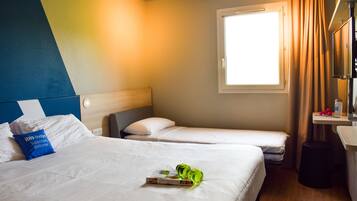 Camera d'albergo con due letti, una finestra con tende, un comodino e uno sgabello.