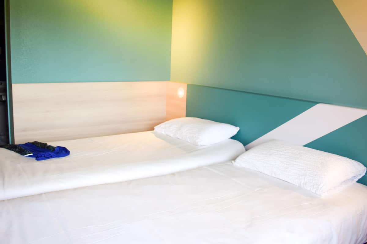 Una cama individual con ropa blanca, cabecera de madera y una pared de acento color verde azulado.