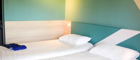 A single bed with white bedding, a wooden headboard, and a teal accent wall.