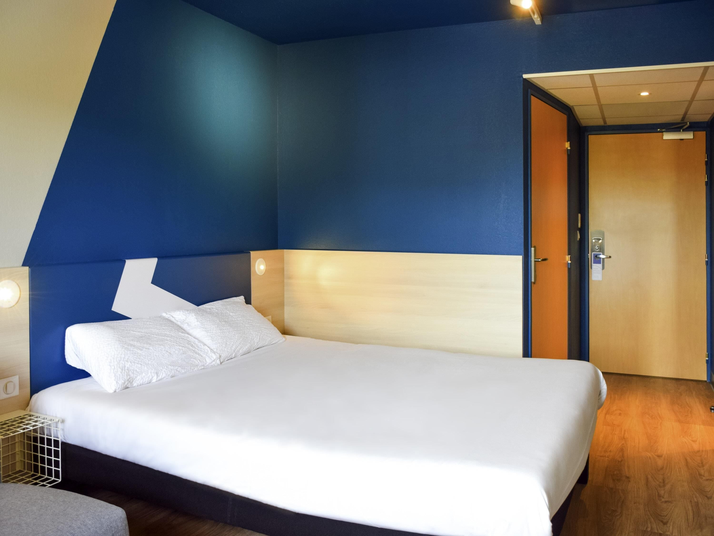 A modern hotel room with a large bed, a wooden headboard, and a blue accent wall.