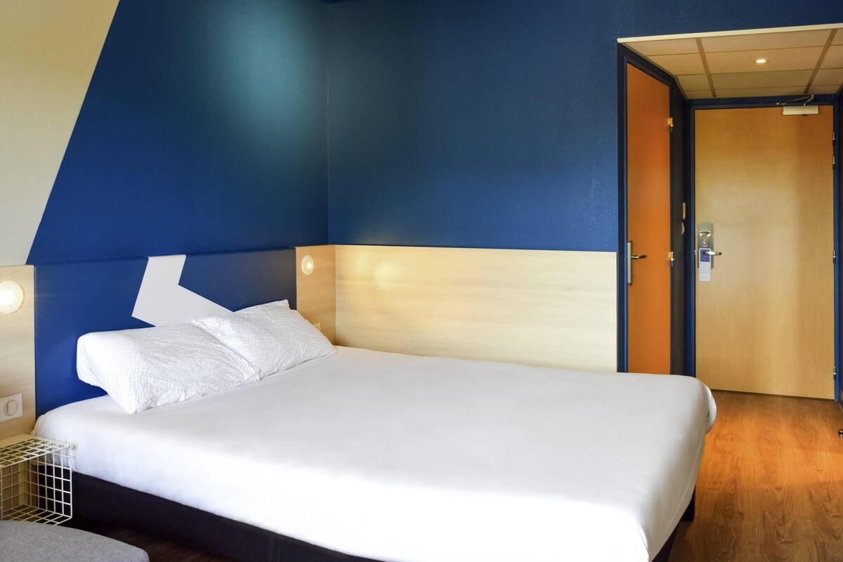 Una habitación de hotel moderna con una cama grande, un cabecero de madera y una pared azul de acento.