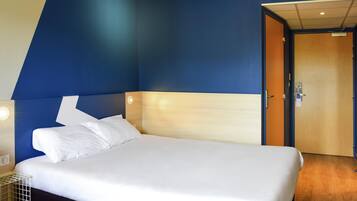 A modern hotel room with a large bed, a wooden headboard, and a blue accent wall.