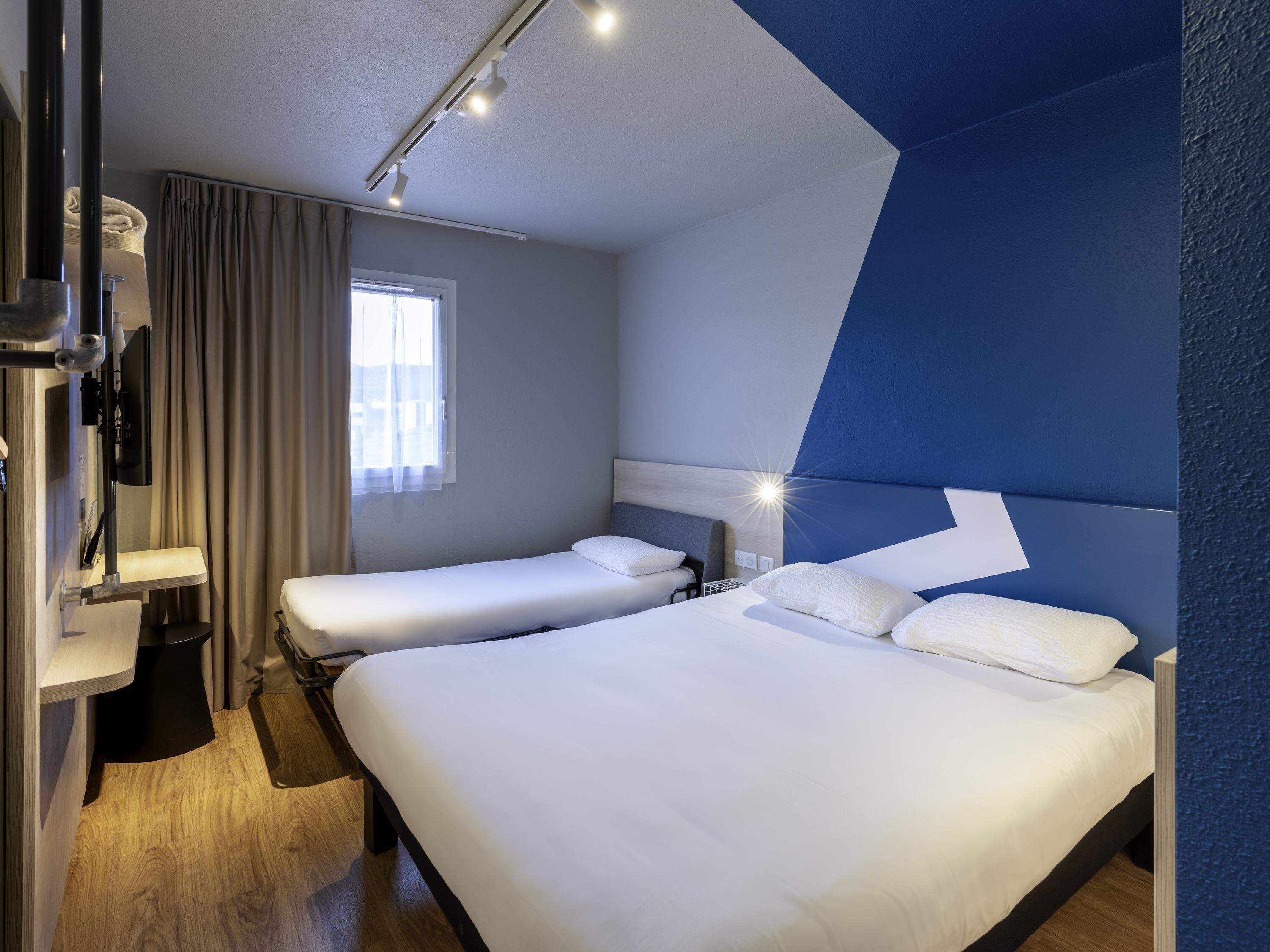 Habitación de hotel con dos camas, un escritorio, una ventana con cortinas y un diseño moderno.