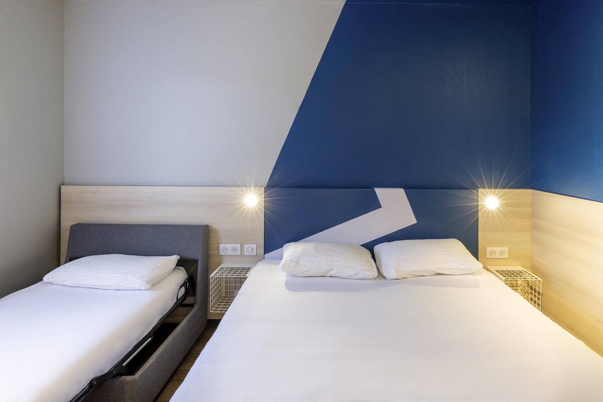 Habitación de hotel con dos camas, cabecero de madera, pared de acento azul y lámparas de noche.