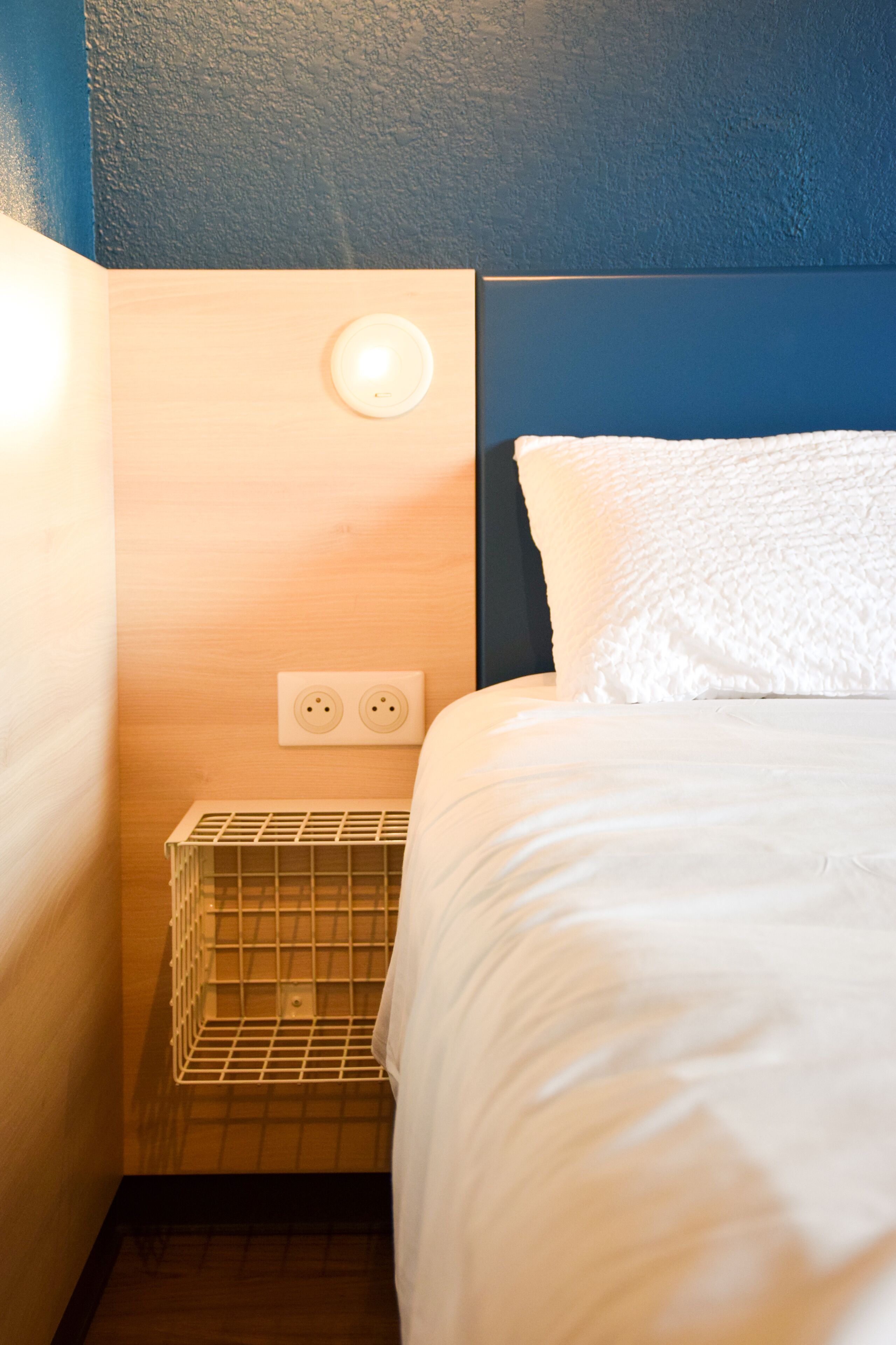 Une chambre d’hôtel équipée d’un lit, d’une table de chevet, d’une prise électrique murale et d’une prise de courant.