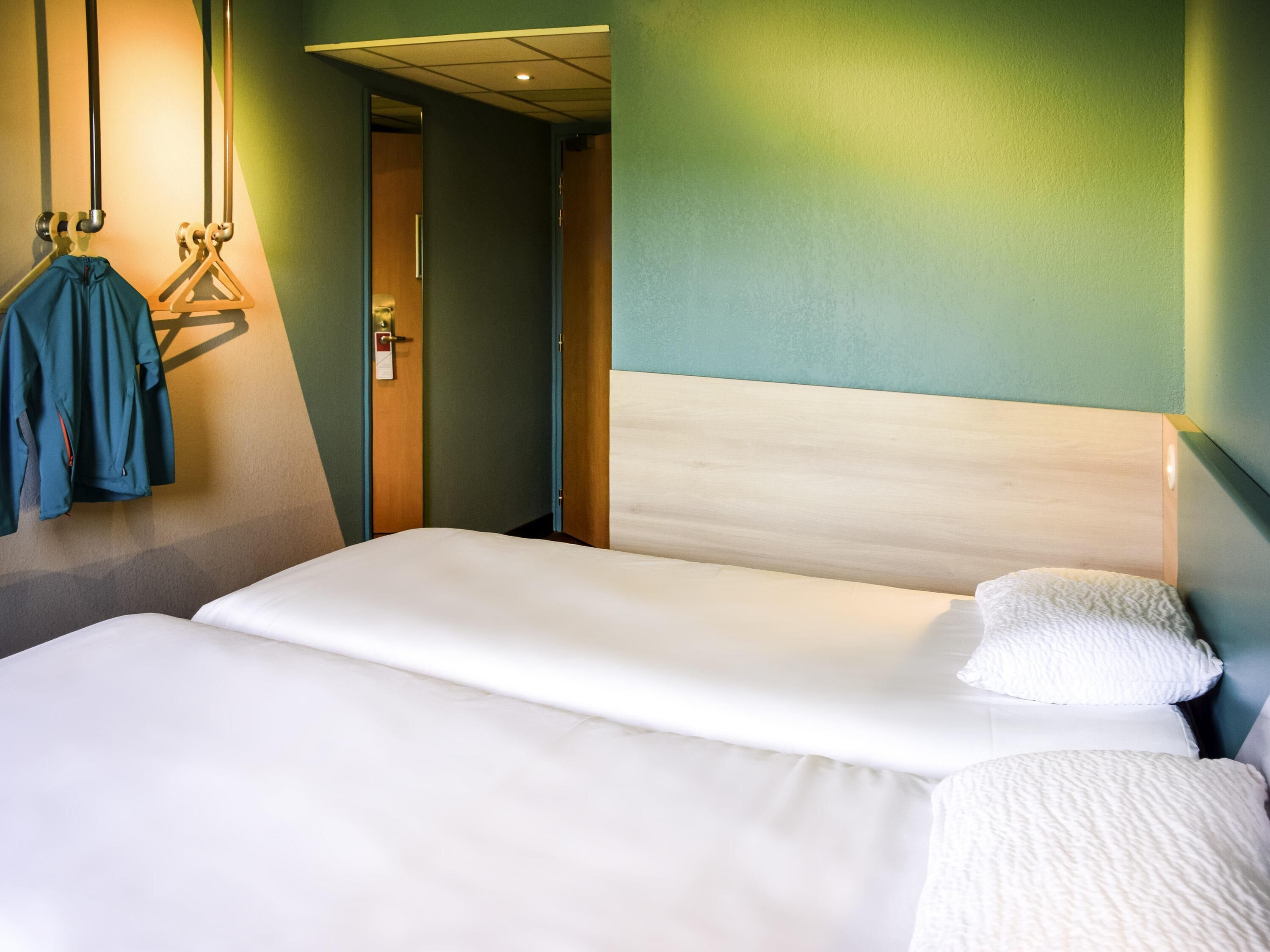 A hotel room with a single bed, a wooden headboard, and a hanging coat rack with a blue garment.