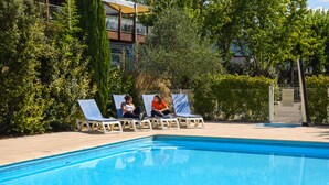 A swimming pool with lounge chairs and a building in the background. - Ibis Budget Millau Viaduc  (Millau)