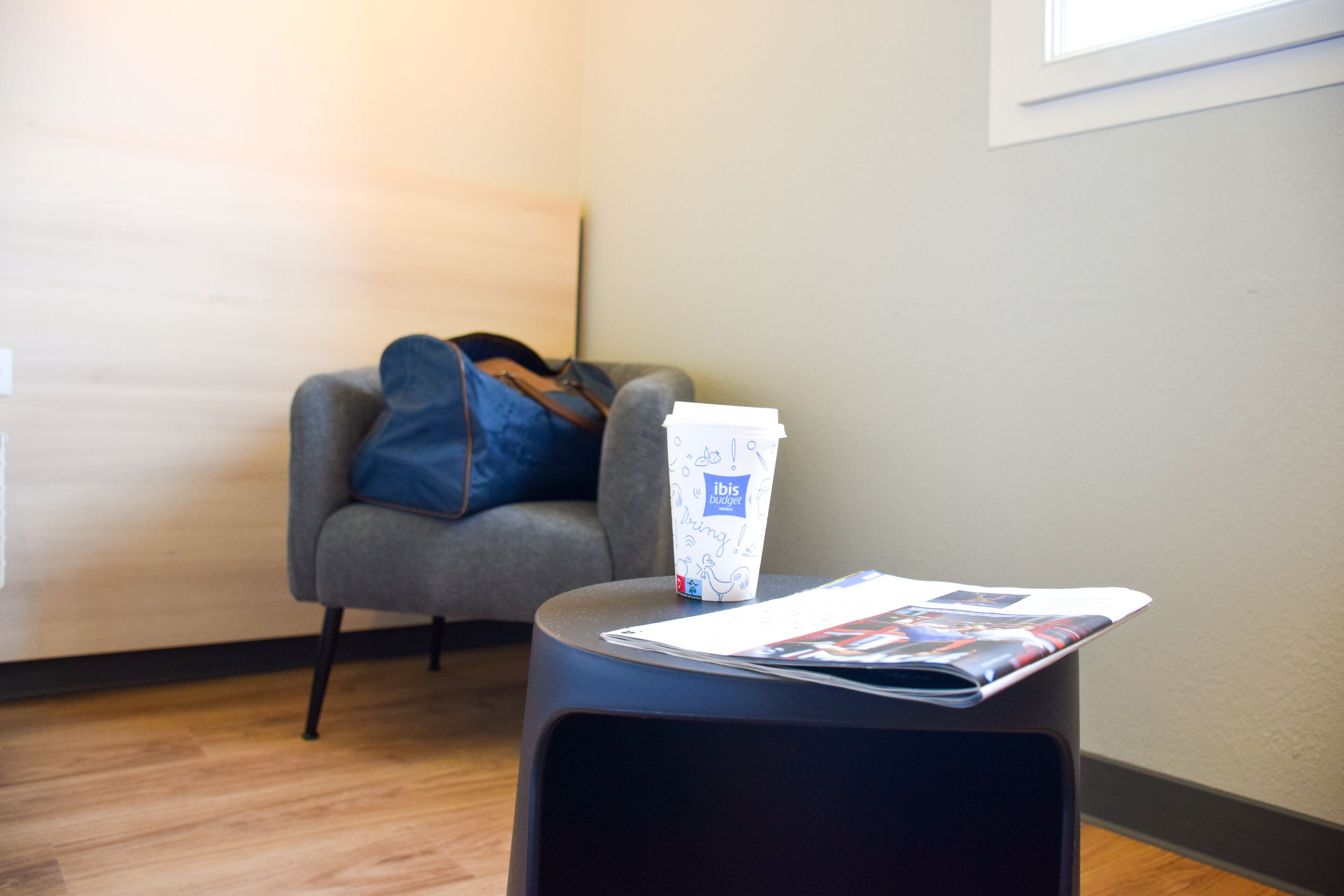 A room with a grey armchair, a small table with a magazine, and a bag on the armchair.