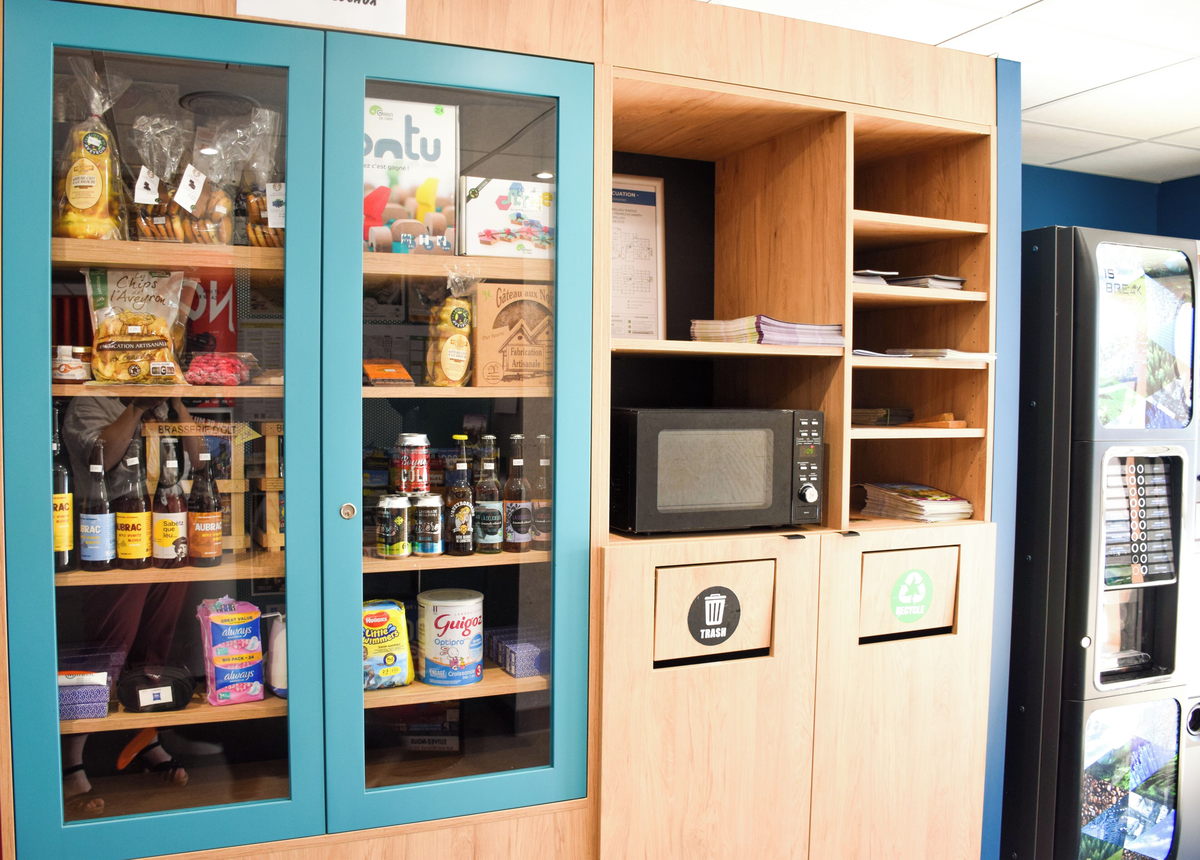 A kitchenette with a microwave, shelves with snacks, and a trash bin.