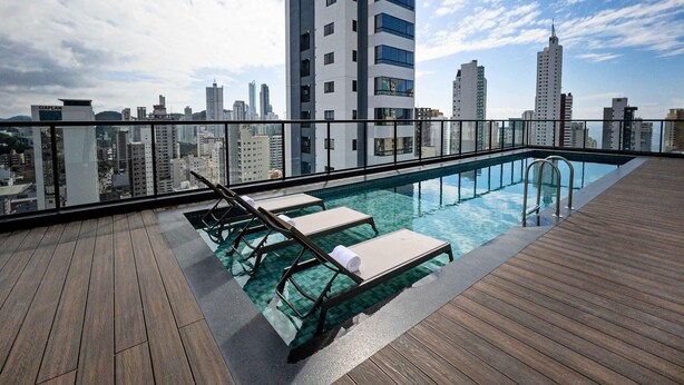 Ein Pool auf dem Dach mit Liegestühlen, einer Holzterrasse und Blick auf die Stadtlandschaft.